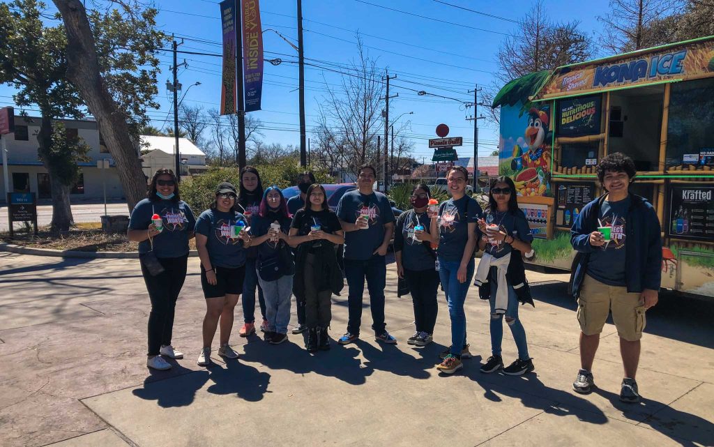 11 volunteers stand in the Witte parking lot, smiling and eating shaved ice.