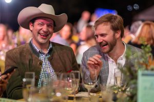 two men sit at a table and laugh.