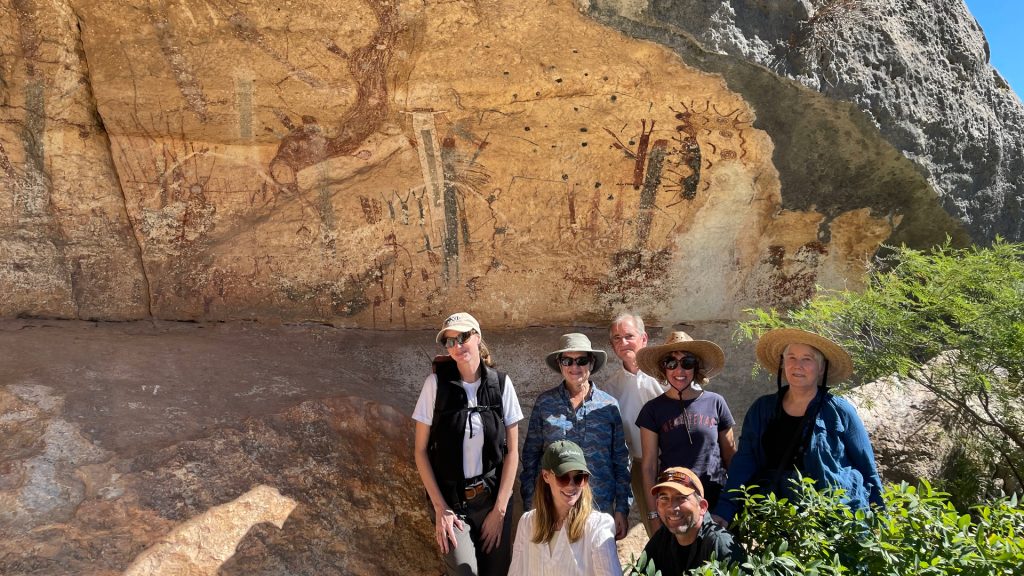 Hikers standing in front of white shaman preserve rock art cliff face.