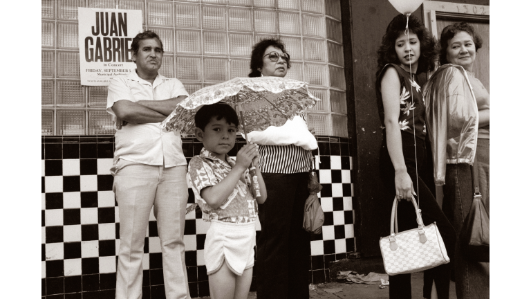 Family standing in front of storefront while child holds umbrella.