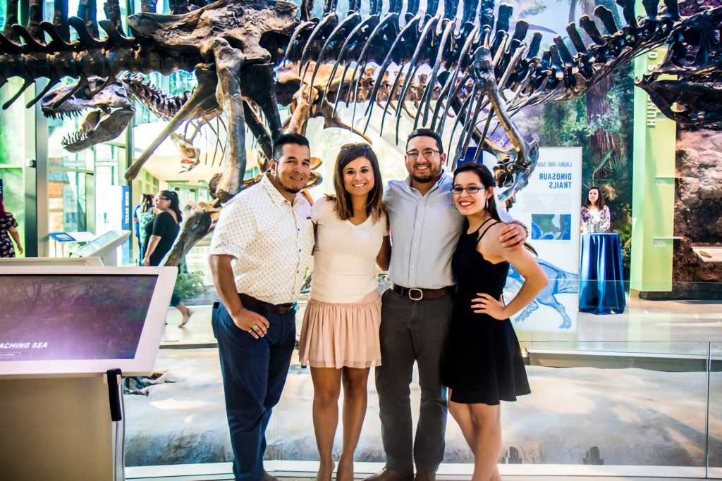 Four adults stand in front of dinosaur