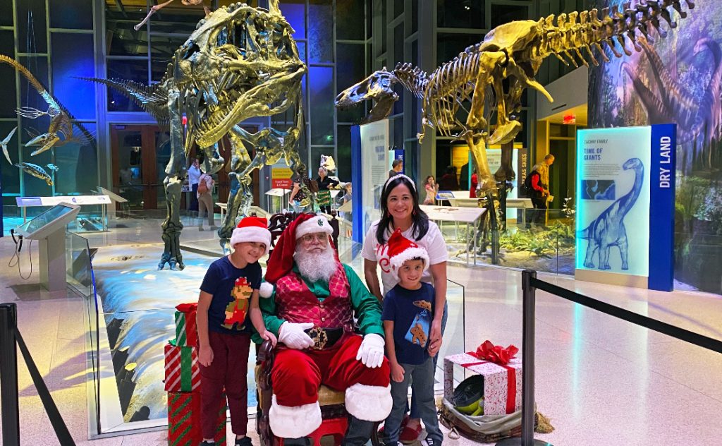 family poses with santa in front of a gallery of dinosaur fossils